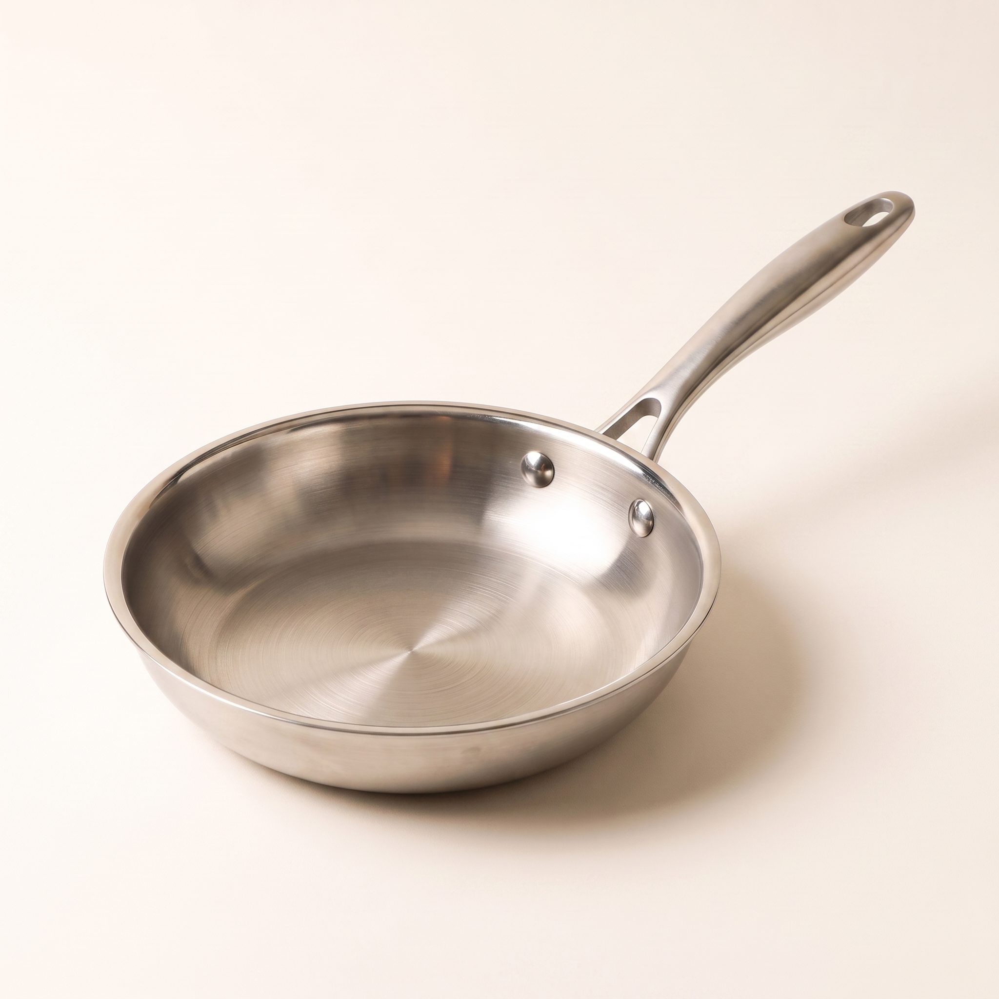 Poêle inox 26 cm Marthe vue de trois quarts, manche riveté, fond blanc beurre